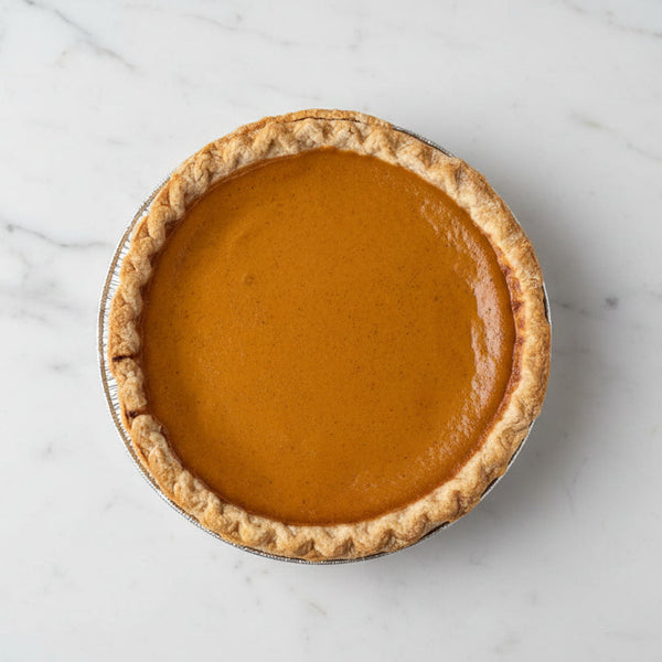 Whole Brown's Market sweet pumpkin pie with smooth orange filling and crimped crust in a foil pan, viewed from above