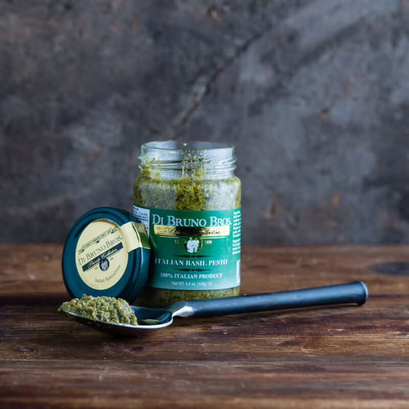 Open jar of Di Bruno Bros. basil pesto beside a spoonful of pesto