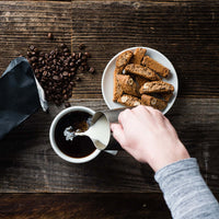 Biscotti on a plate beside coffee as cream is poured into a cup