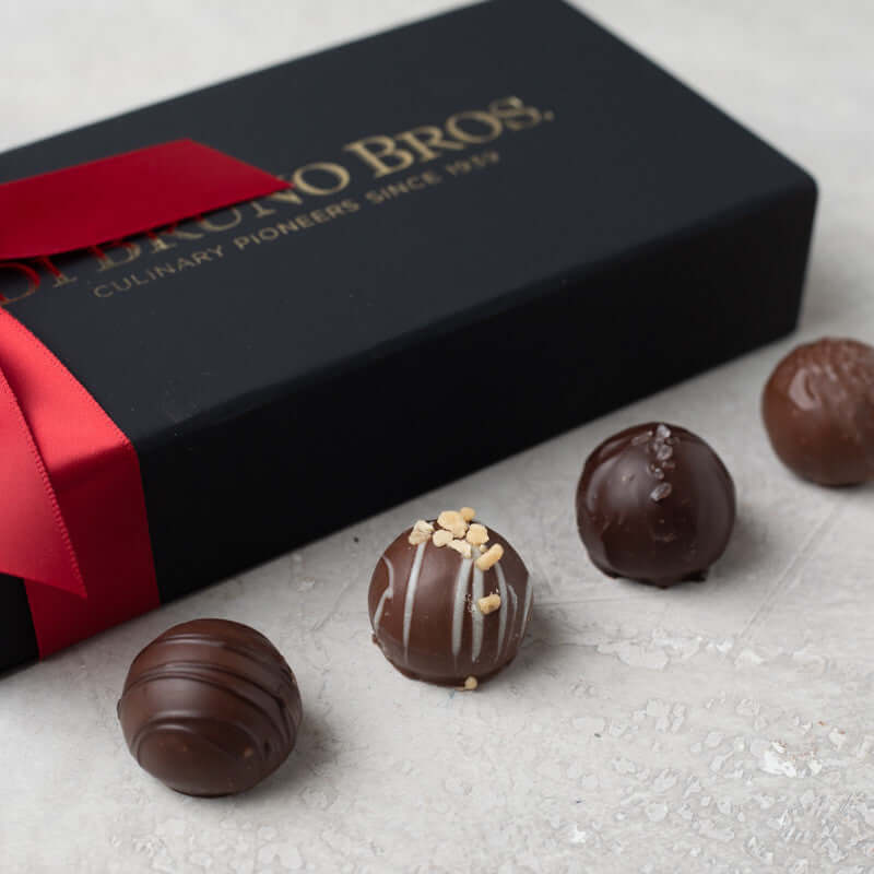 Four assorted Di Bruno Bros. chocolate truffles beside a black gift box with a red ribbon
