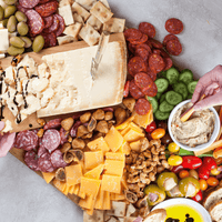 Overhead serving spread with cheeses, sliced cured meats, olives, crackers, vegetables, and dips