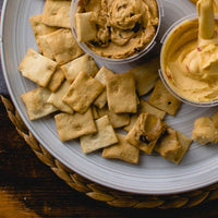 Crostini crackers and two open cheese spread containers on a white serving plate