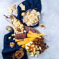 Styled round cheese and charcuterie board with sliced cheeses, salami, crostini, spreads, honey, fruit, and nuts