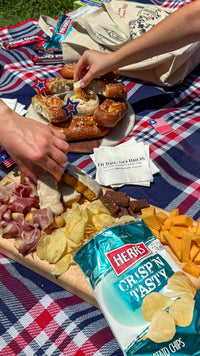 Picnic serving scene with pretzels, dip, deli foods, and Herr’s chips; some foods shown are not in the gift bag