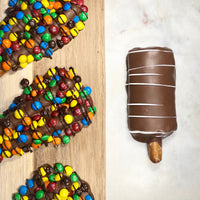 Candy-covered and peanut butter gluten-free chocolate pretzel rods shown on wood and marble surfaces