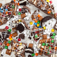Chocolate bark pieces topped with pretzels, caramel, marshmallows, colorful candy pieces and chocolate cookies